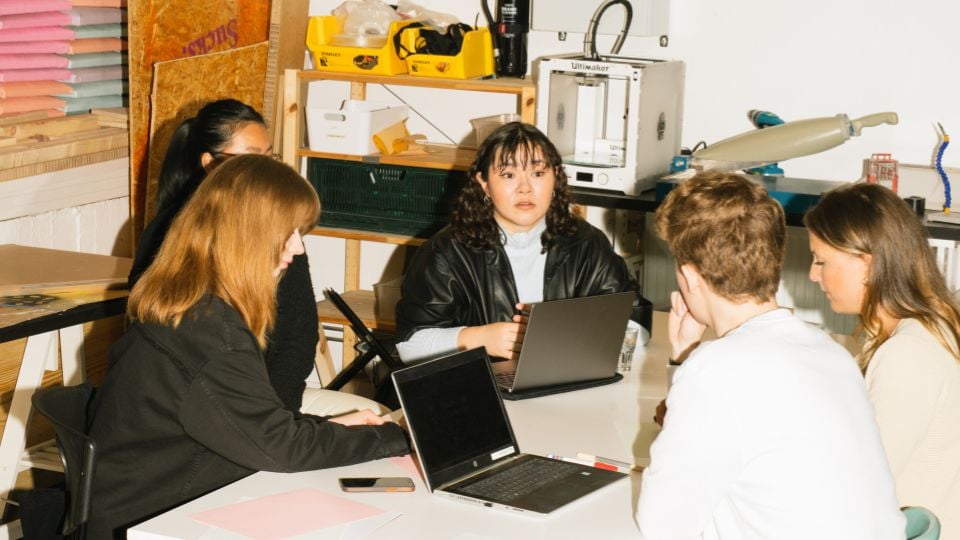 Five people sitting around a desk with open laptops, engaged in a discussion.