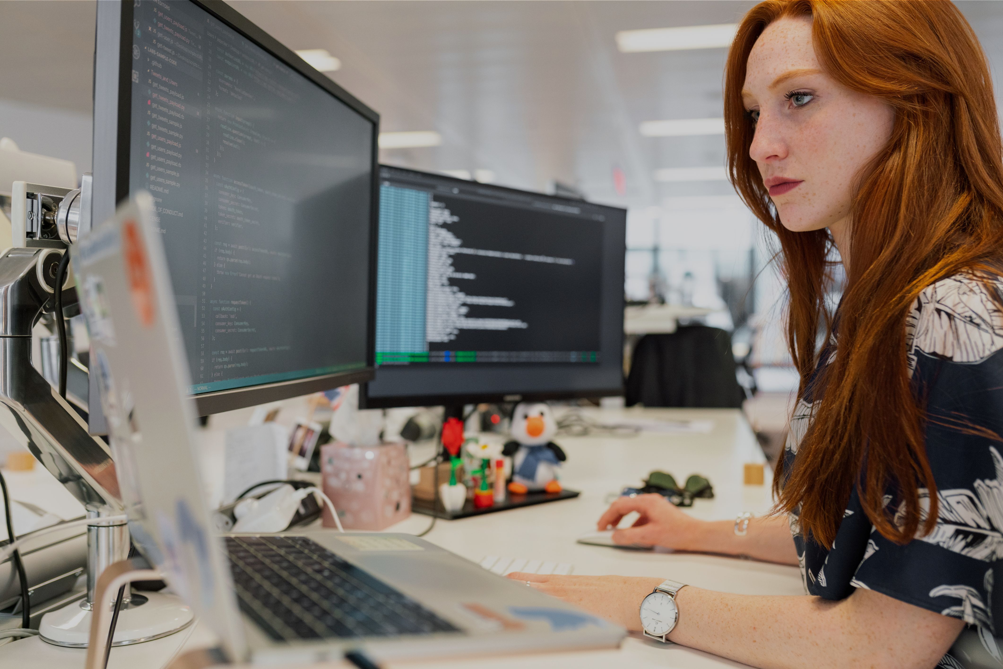 A developer intently reviews lines of code on her dual-monitor setup, representing the technical work behind implementing AI solutions across industries.