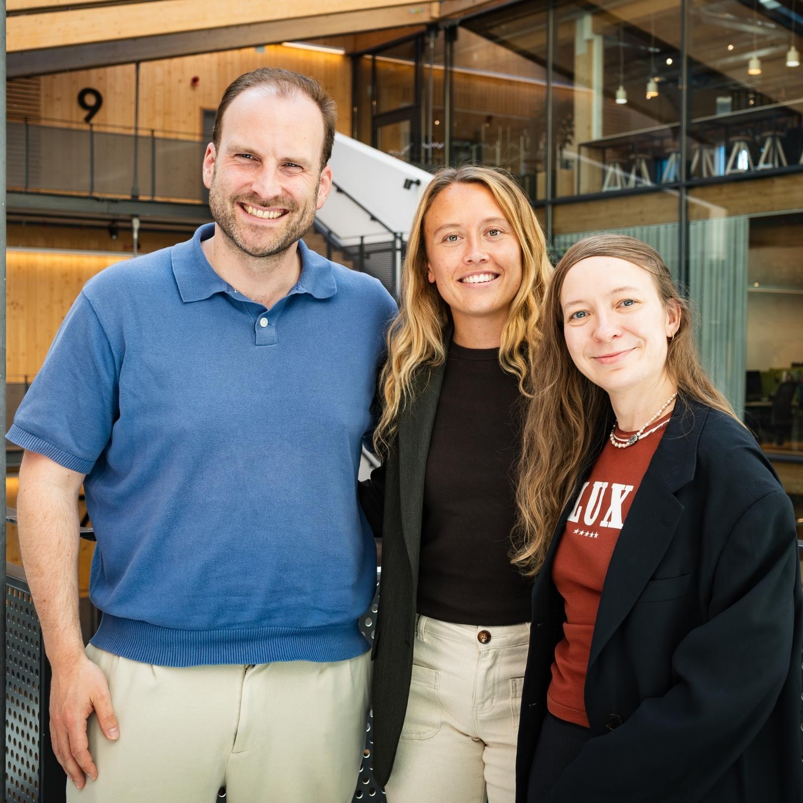 Wessel from Miro, Linn from Hyper Island, and Anna from Miro standing together and smiling at the camera in a modern office building.