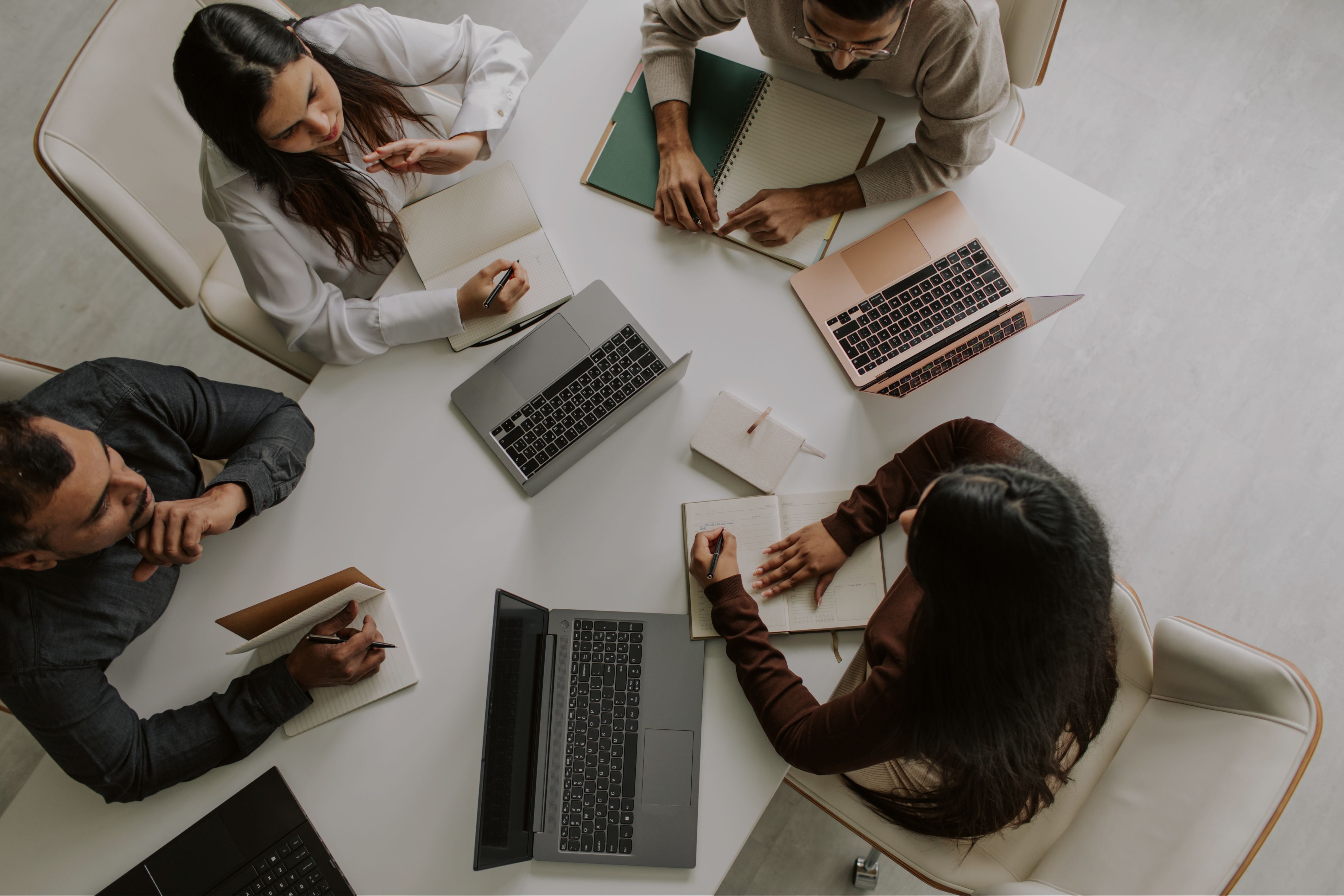 An overhead view of a team collaborating around a table, using leadership tools like laptops and notebooks for a strategic planning session.