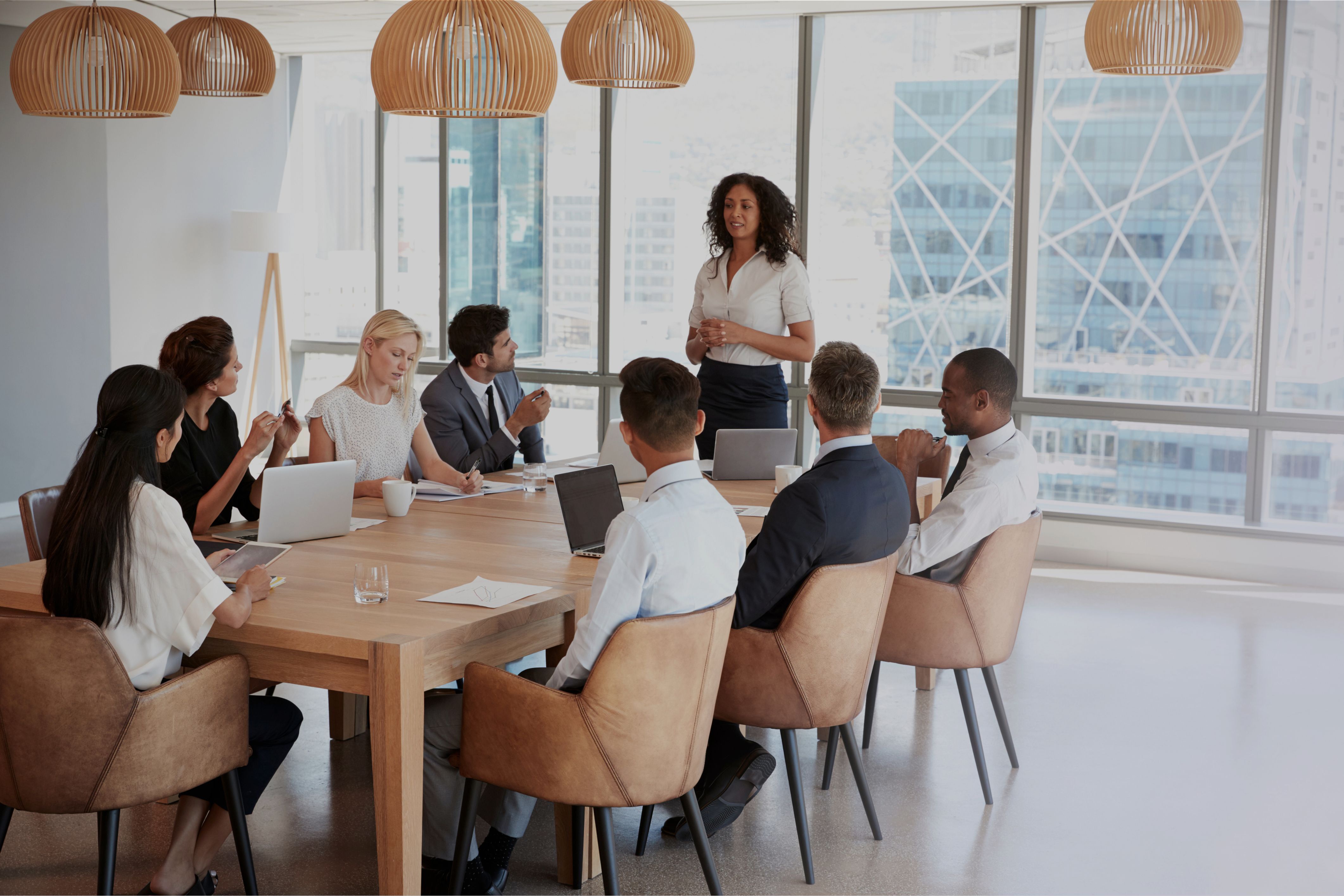 A smiling woman holding a pen and notebook facilitates an interactive group discussion, showing good meeting engagement.