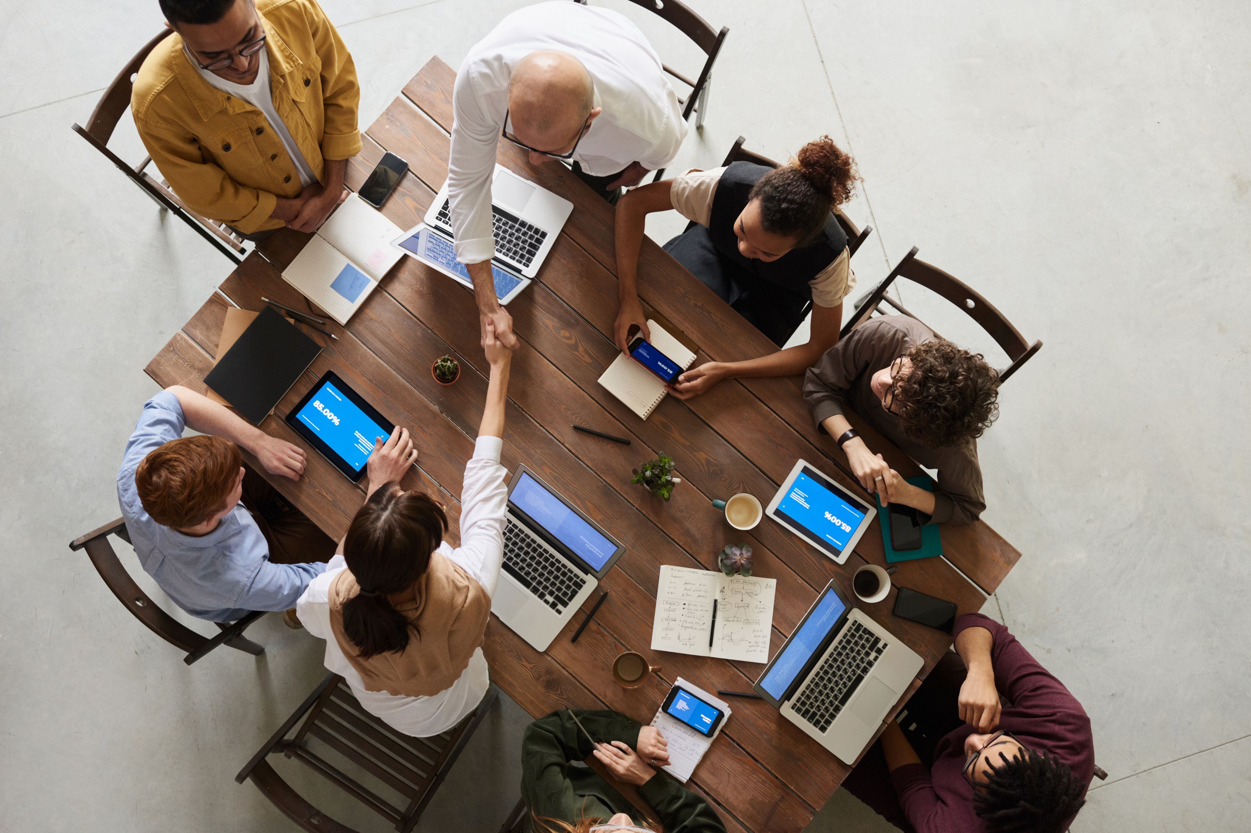 Top-down view of a successfully facilitated workshop, where reaching an agreement is symbolized by a handshake between participants in the center of the table.