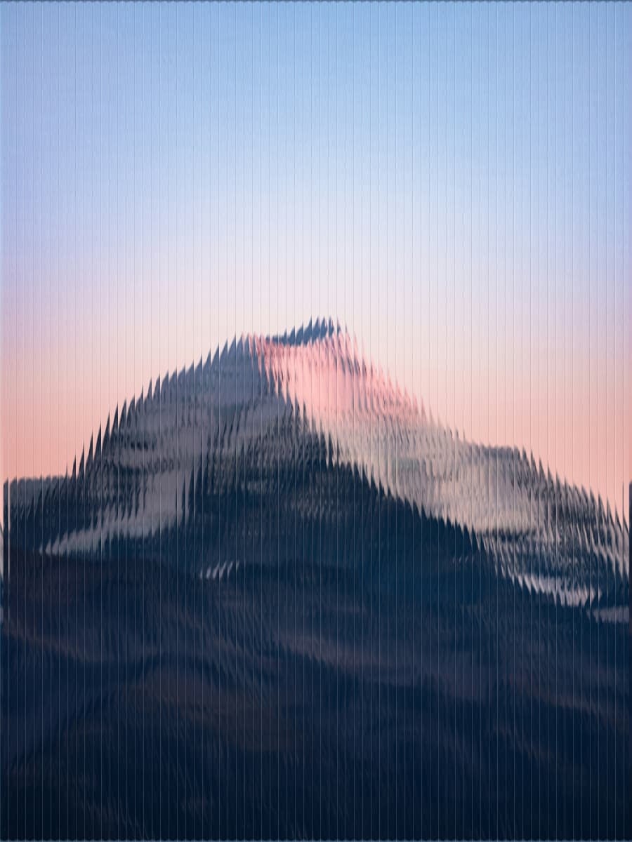 Mountain landscape distorted through textured glass, with a soft blue and pink sky in the background.